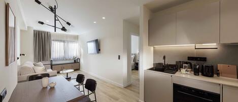 Una cocina moderna con horno integrado, un comedor con mesa y sillas de madera, y una sala de estar con sofá y televisor.