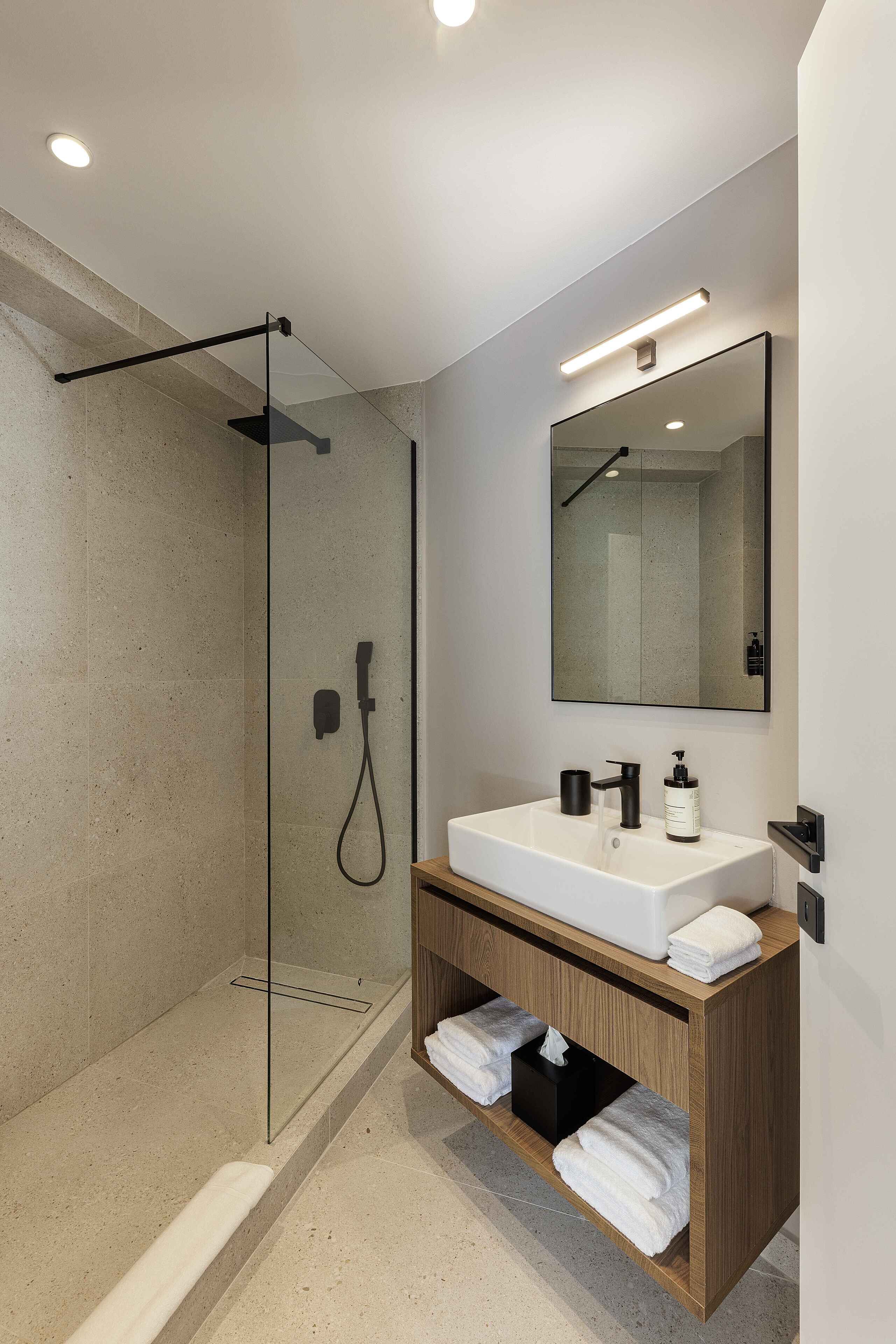 A modern bathroom with a glass-enclosed shower, a white sink with a wooden vanity, and a mirror above the sink.