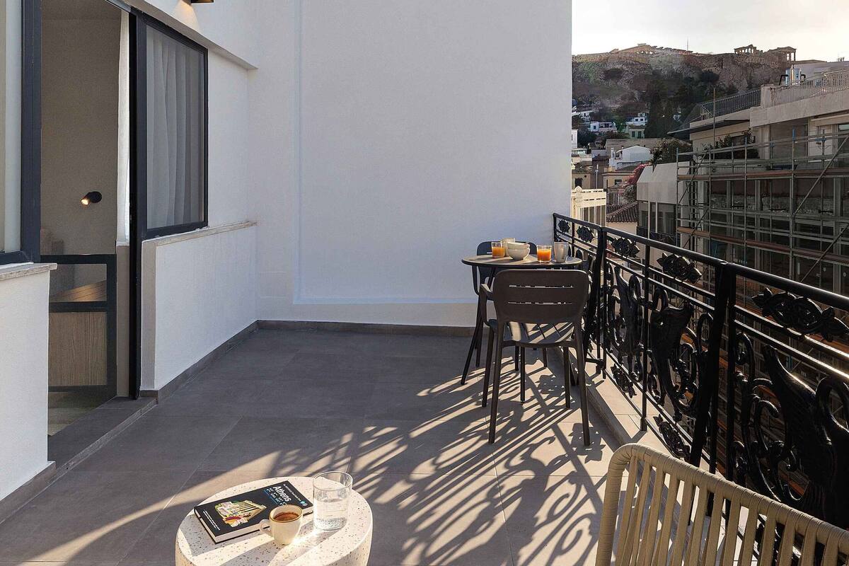 Ein Balkon mit einer weißen Wand, einem kleinen Tisch mit Buch und Glas sowie einem Stuhl.