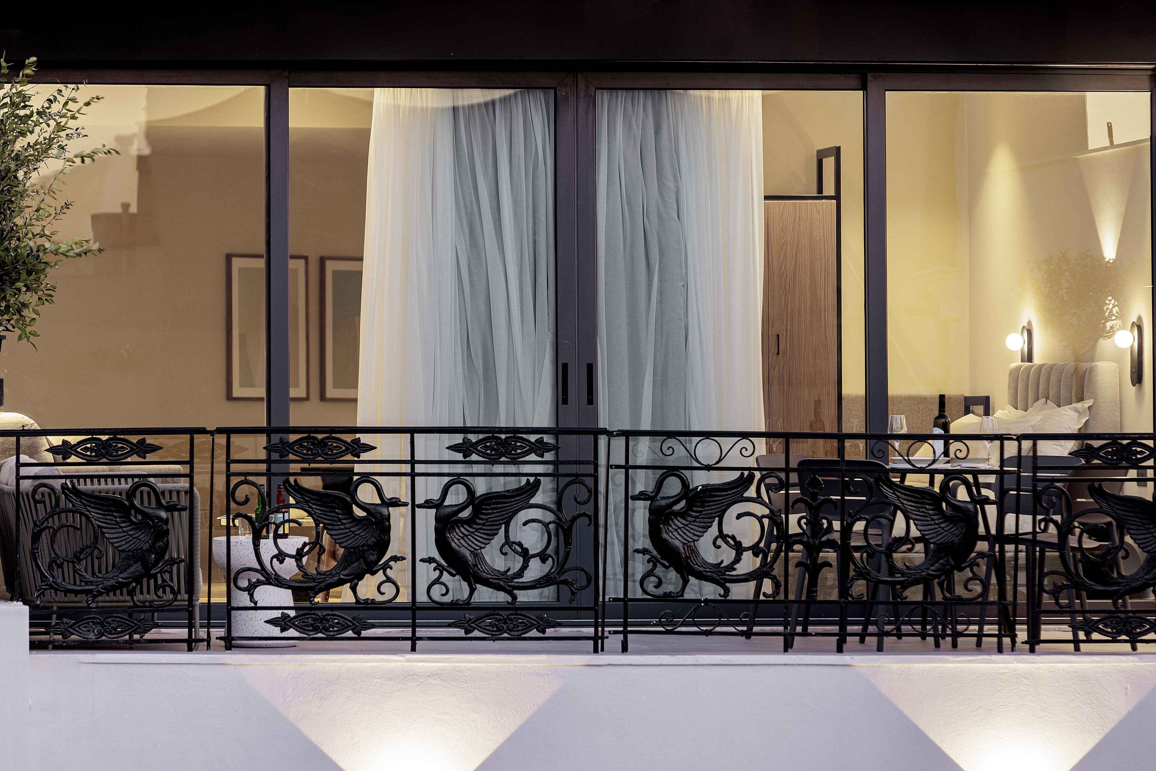 A balcony with ornate metal railings and a seating area with chairs and tables.