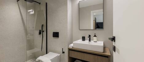 A modern bathroom with a glass-enclosed shower, a white sink with a wooden vanity, and a large mirror.