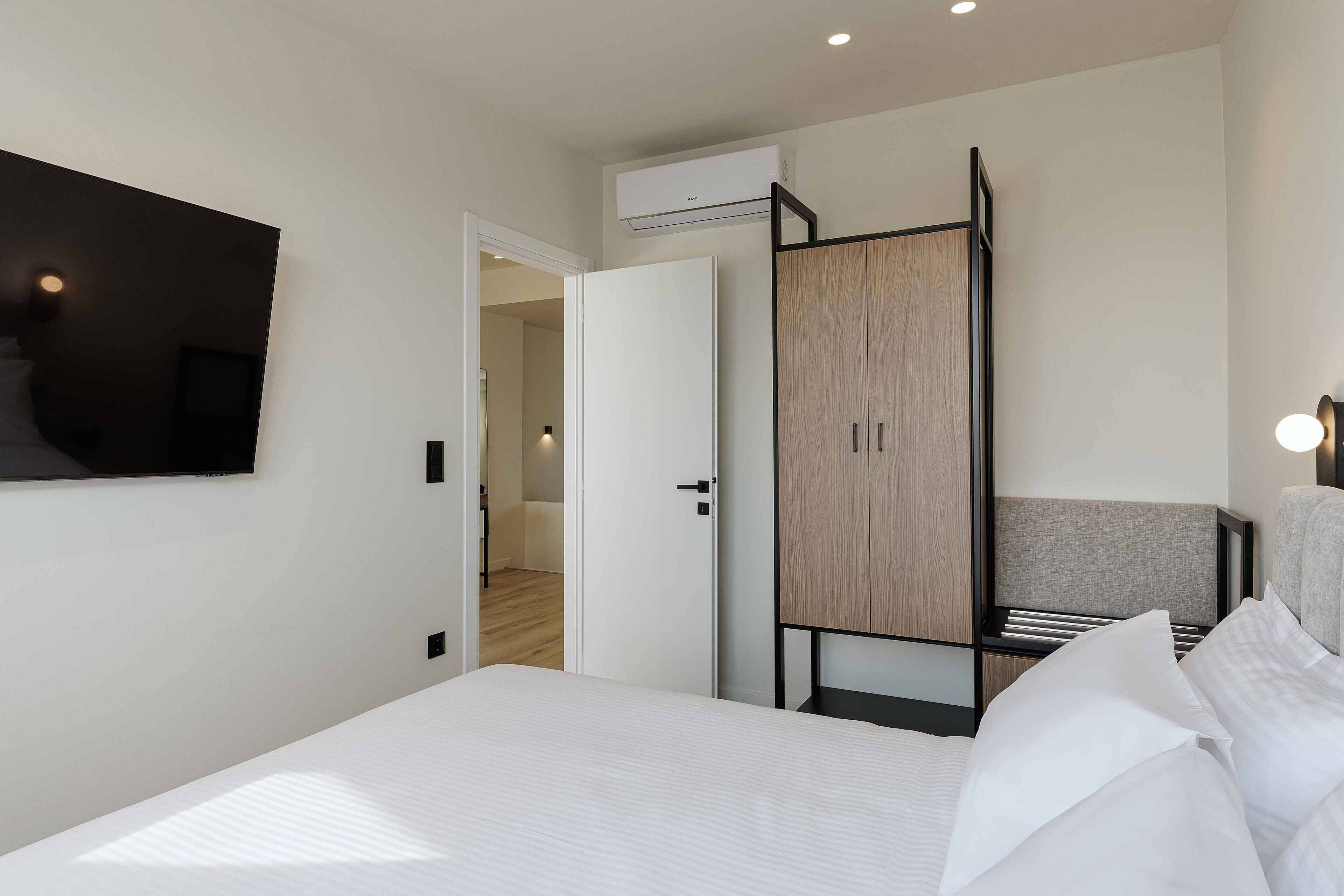 A modern hotel room with a large bed, a wardrobe, a TV mounted on the wall, and an air conditioning unit.