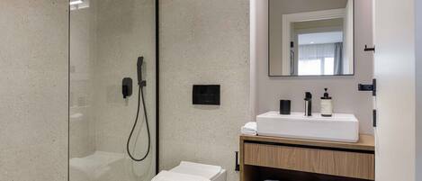 Ein modernes Badezimmer mit einer Duschkabine, einer weißen Toilette, einem Holz-Waschtisch mit Spiegel und ordentlich gefalteten Handtüchern.