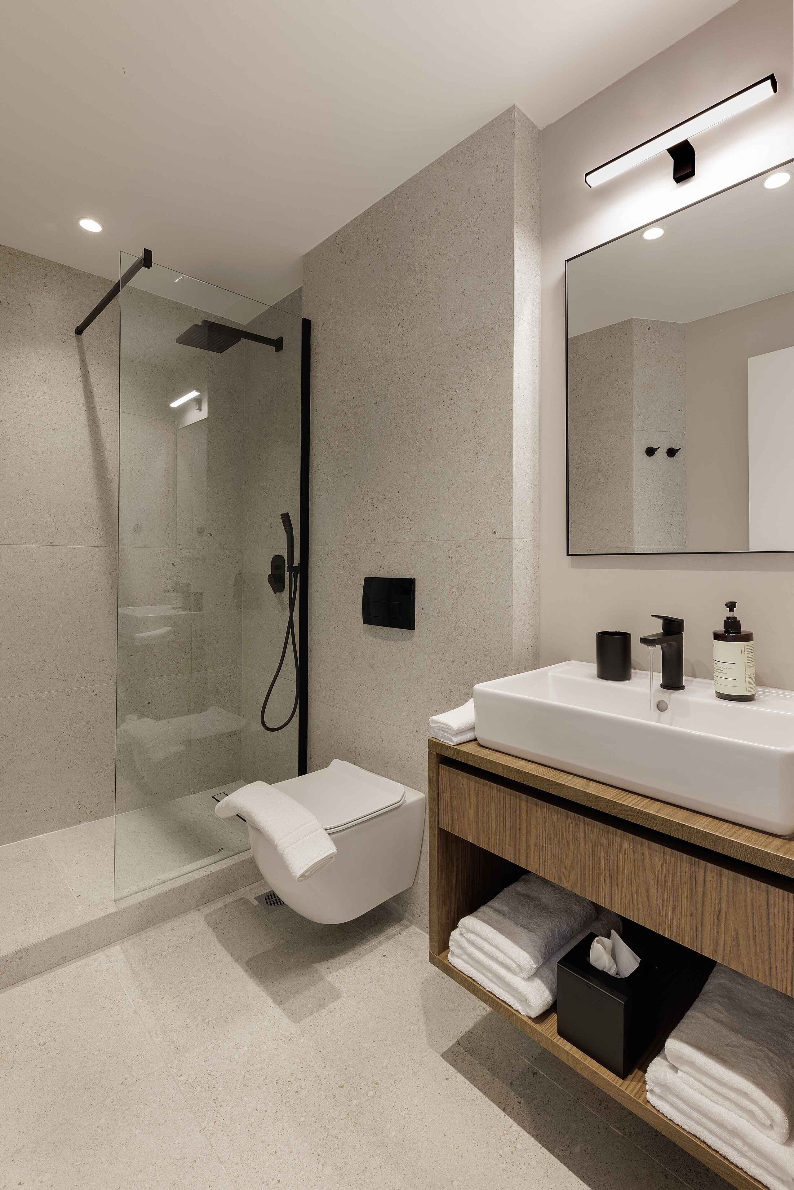 A modern bathroom with a glass-enclosed shower, a white sink with a wooden vanity, and a large mirror.