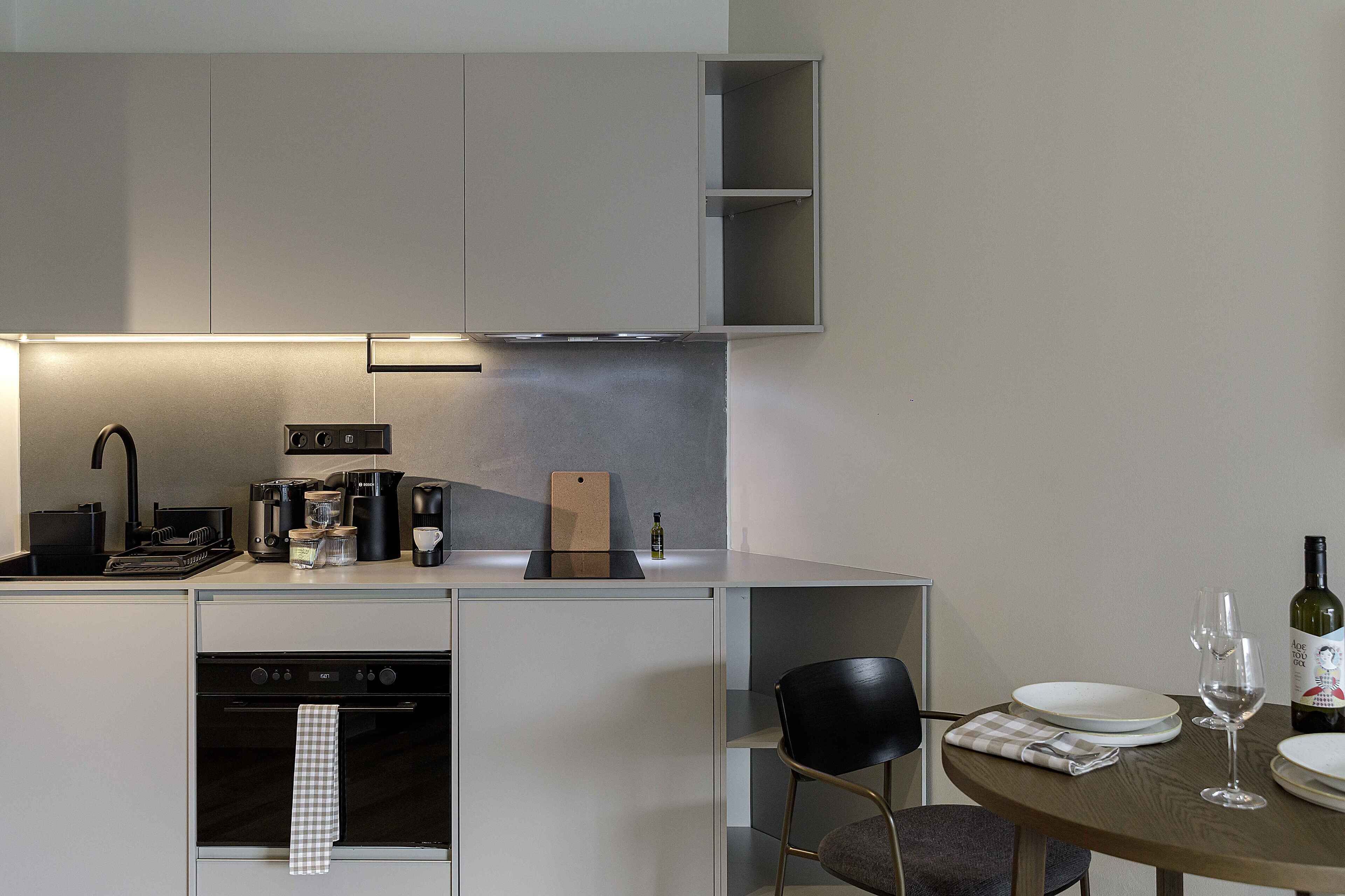 A compact kitchen with modern appliances, a dining area with a table and chairs, and a wine bottle on the table.