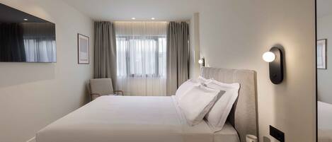 A modern hotel room with a large bed, a bedside table with a lamp, a chair, and a window with curtains.