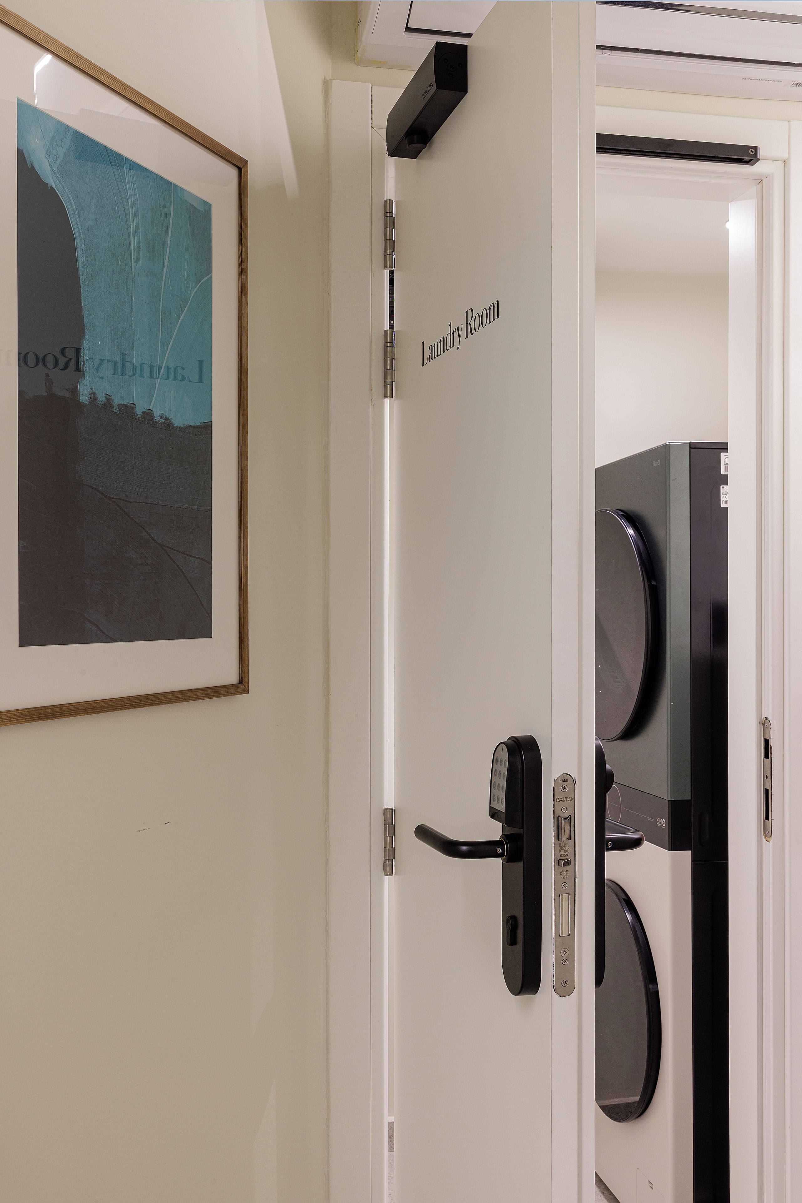 Una puerta con el letrero 'Laundry Room' y un moderno picaporte, además de un objeto negro en el marco de la puerta.