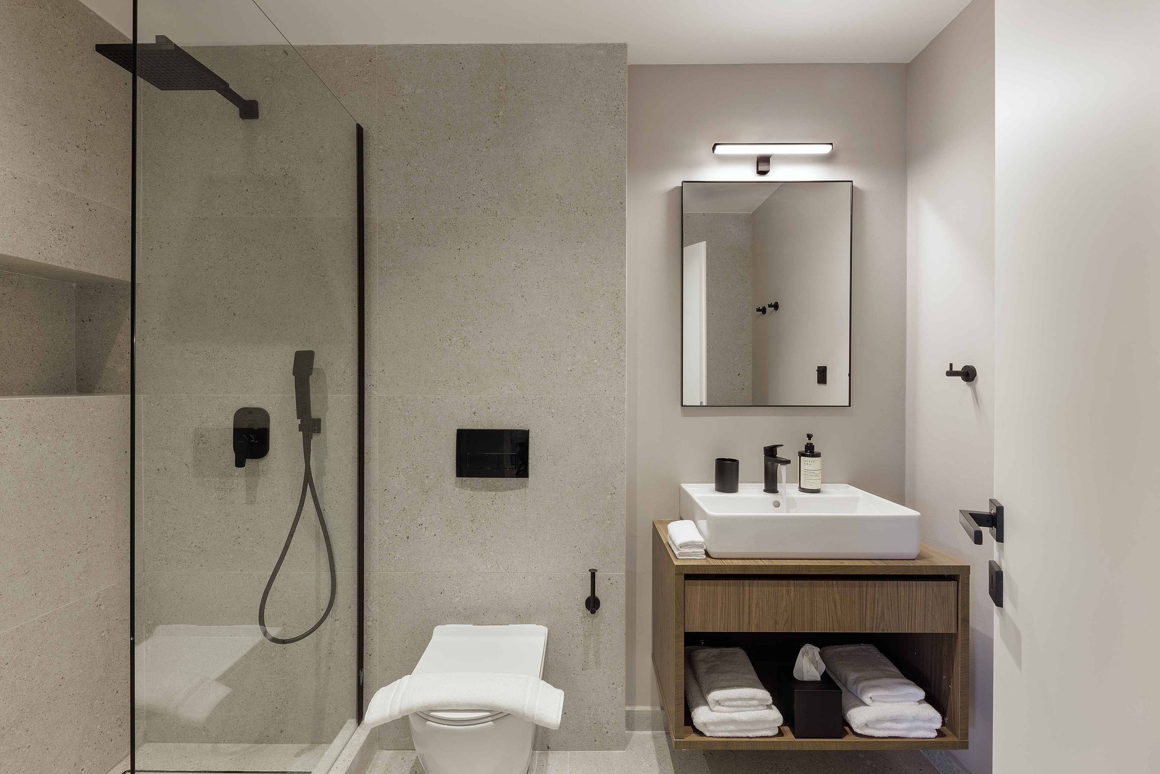 Un baño moderno con ducha de vidrio, inodoro blanco, tocador de madera con lavamanos y espejo sobre el tocador.