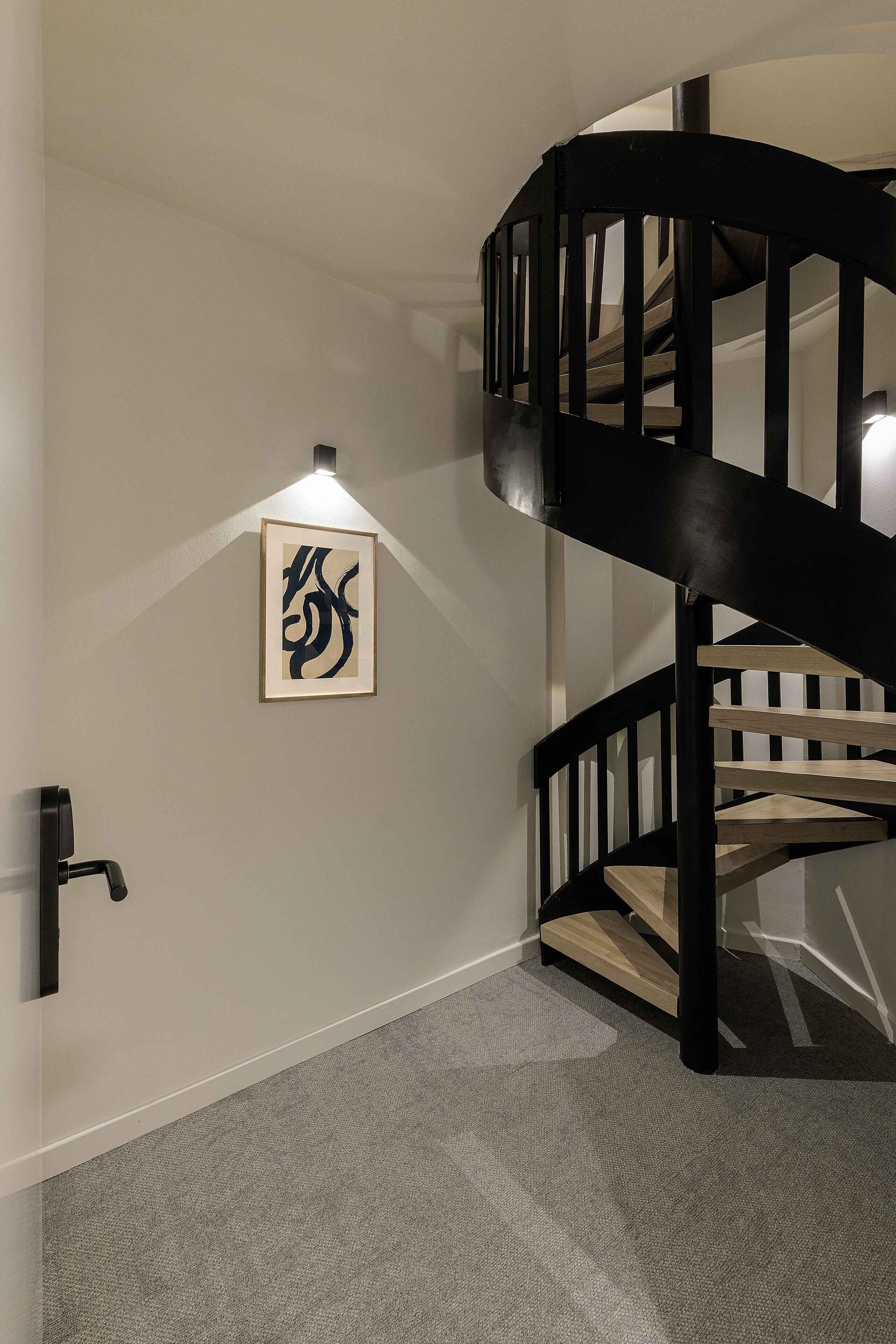 Un escalier avec une rampe noire et une œuvre d’art encadrée accrochée au mur.