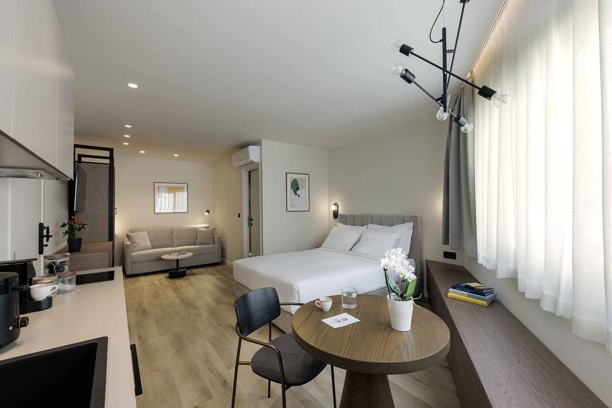 Ein modernes Hotelzimmer mit Bett, Sofa, Esstisch und Küchenzeile.