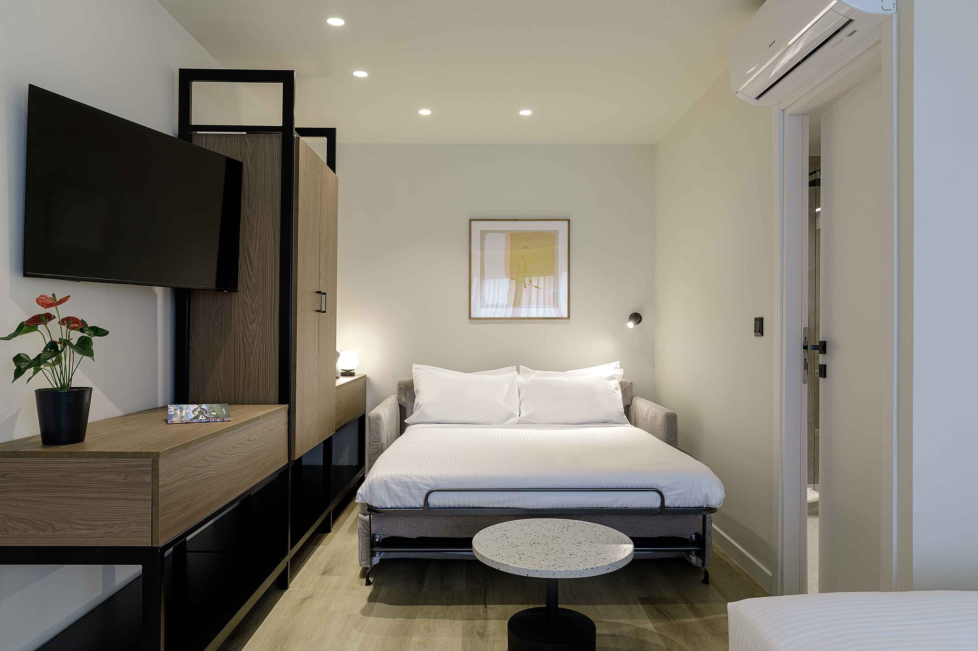 A modern hotel room with a bed, bedside table, TV, and a small round table.