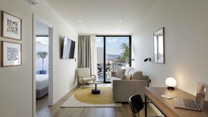 Habitació d'hotel moderna amb terra de fusta, un sofà, escriptori amb un ordinador portàtil, televisió i un balcó amb vistes a la ciutat.