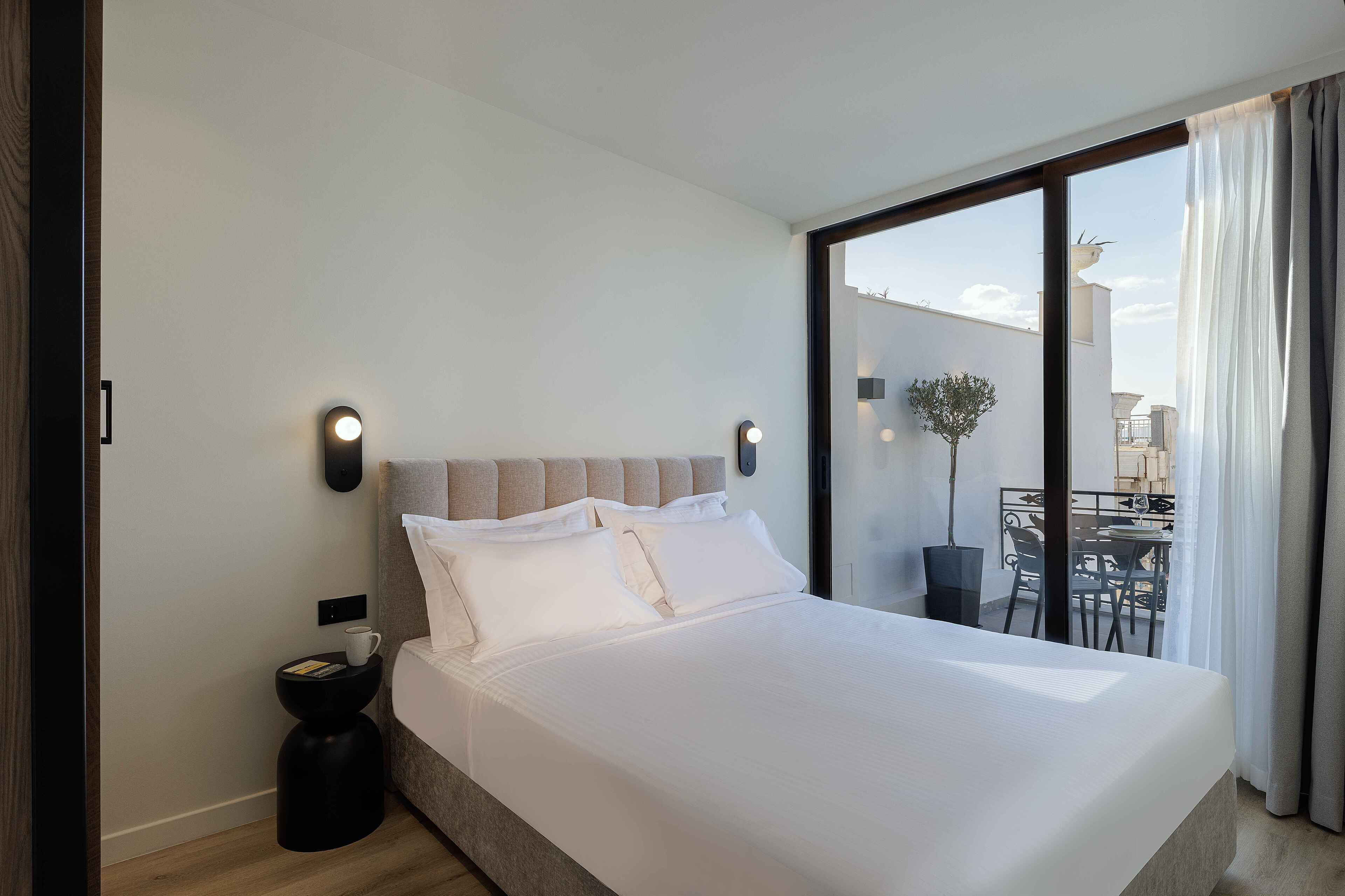 Ein modernes Hotelzimmer mit einem großen Bett, einem kleinen Nachttisch und Blick auf den Balkon.