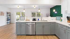 A modern kitchen with grey cabinets, a stainless steel dishwasher, pendant lights, and a green wall accent.