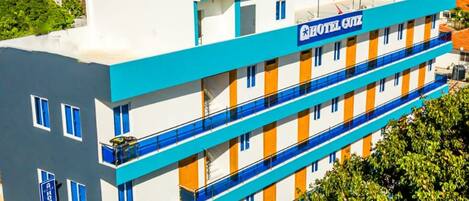 Un hotel de varios pisos con fachada azul y blanca, balcones en cada planta y vista al océano.
