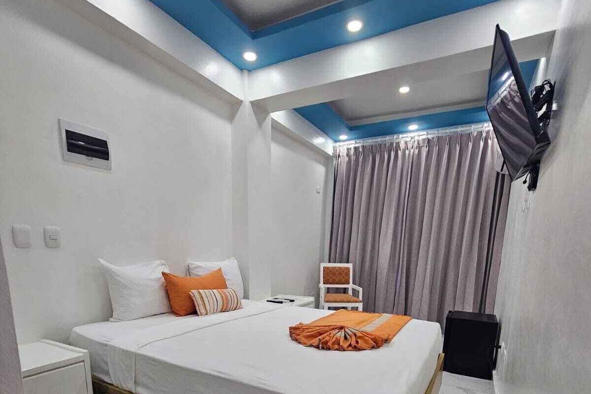Een moderne hotelkamer met een houten bedframe, witte beddengoed en een wandgemonteerde flatscreen televisie.