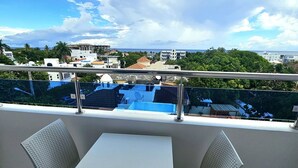 En balkon med et hvidt bord og to stole, der giver udsigt over bybilledet med bygninger og en klar himmel.
