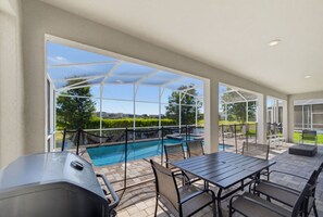 An outdoor patio with a pool, seating area, and grill.