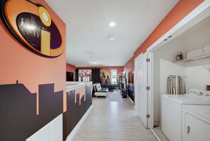 A hallway with a cityscape mural, a laundry area with a washing machine, and a seating area with a sofa and a chair.