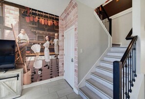A staircase with a black handrail and white steps, leading to a room with a brick wall and a mural of chefs.