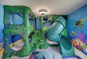 Une salle de jeux avec un toboggan, des murs d’escalade et une fresque représentant une tortue.