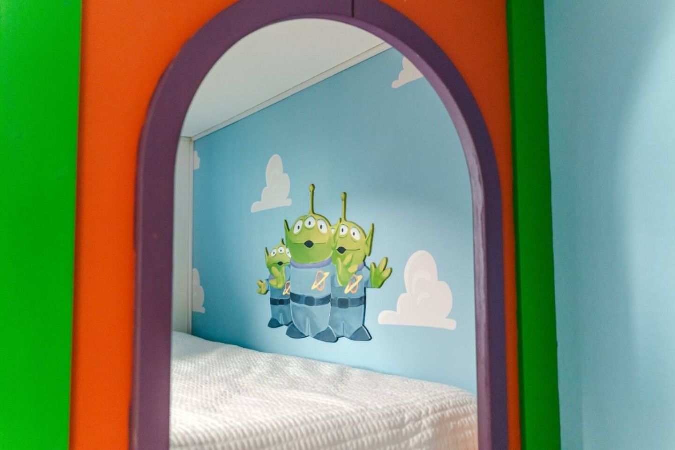 A child's bedroom with a bed, a wall mural of green alien characters, and an archway.