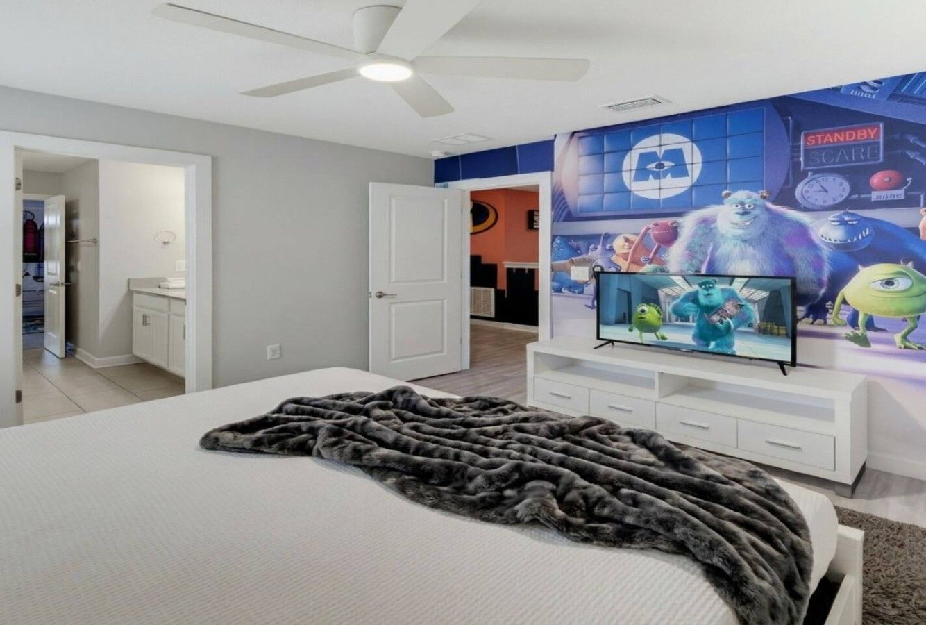 A bedroom with a bed, a television, and a wall with animated characters.