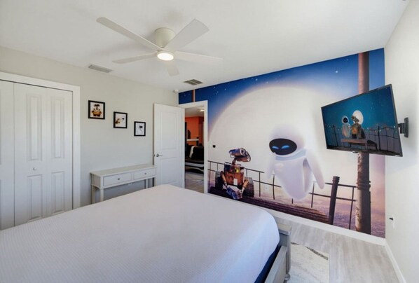 A bedroom with a large bed, a ceiling fan, and a wall mural of a space scene.