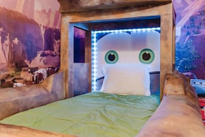 A bed with a green bedspread, a white pillow, and a headboard with LED lights.