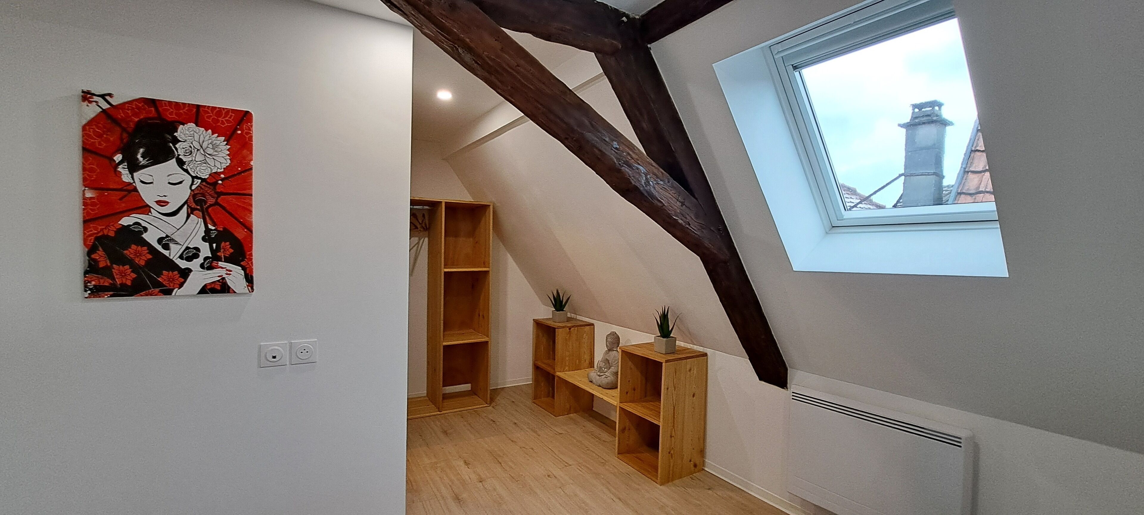 A room with a sloped ceiling, wooden beams, a skylight, and a traditional Japanese artwork on the wall.