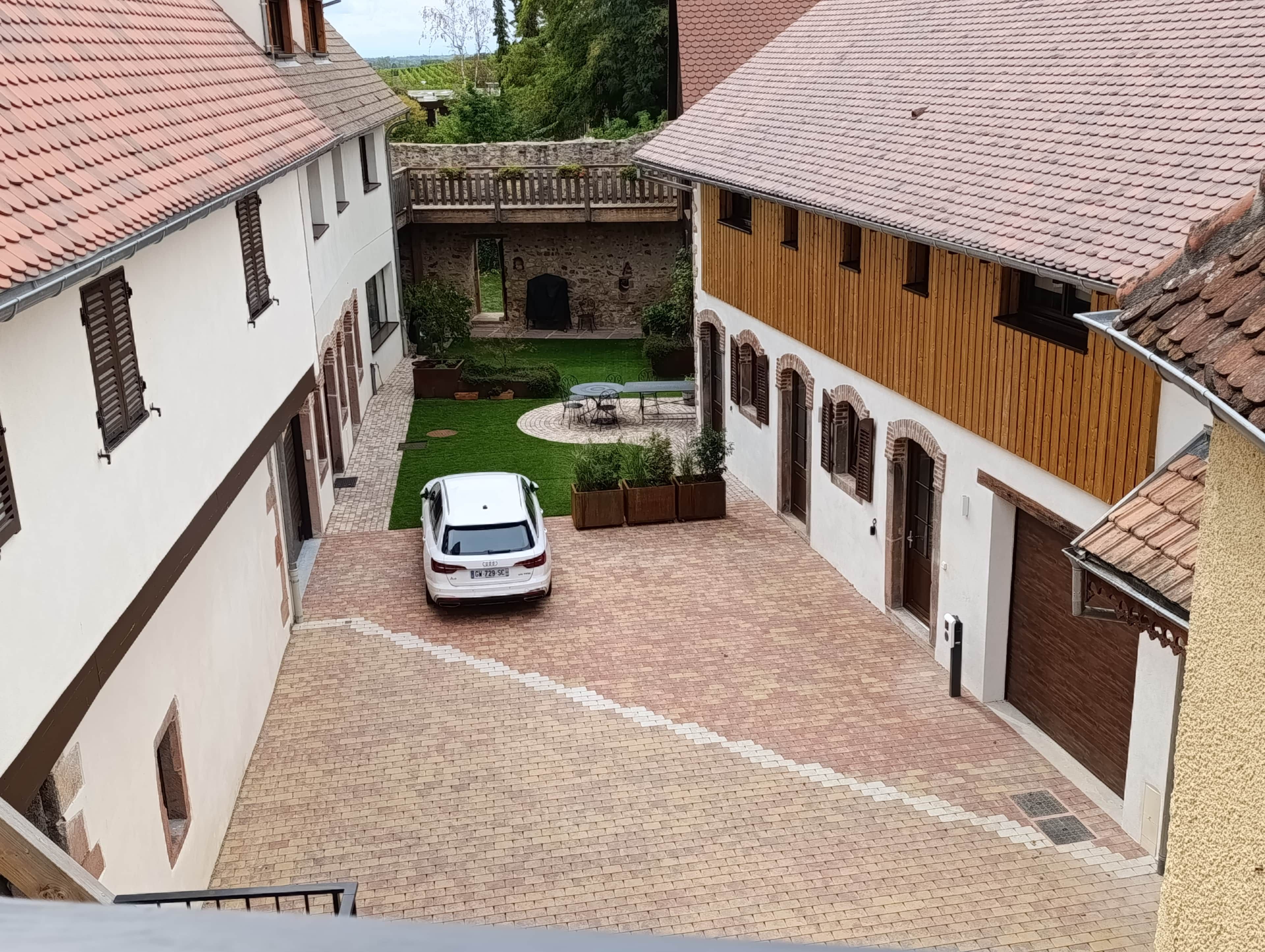 A courtyard with a paved walkway, a white car parked in the center, and buildings with traditional architecture.