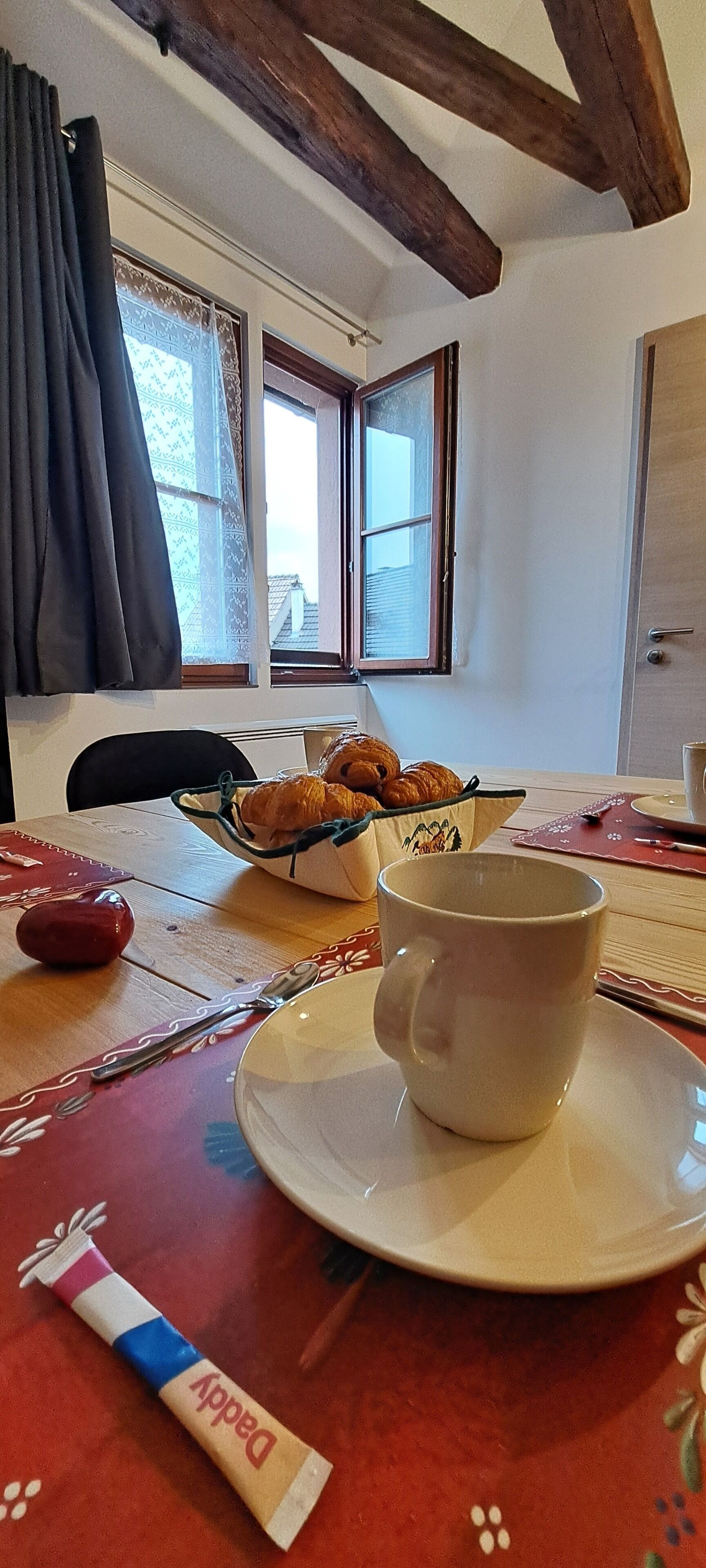 Une table à manger avec une tasse, une assiette et un panier de croissants.