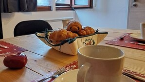 Una mesa de comedor con una taza, un plato y una cesta de cruasanes.