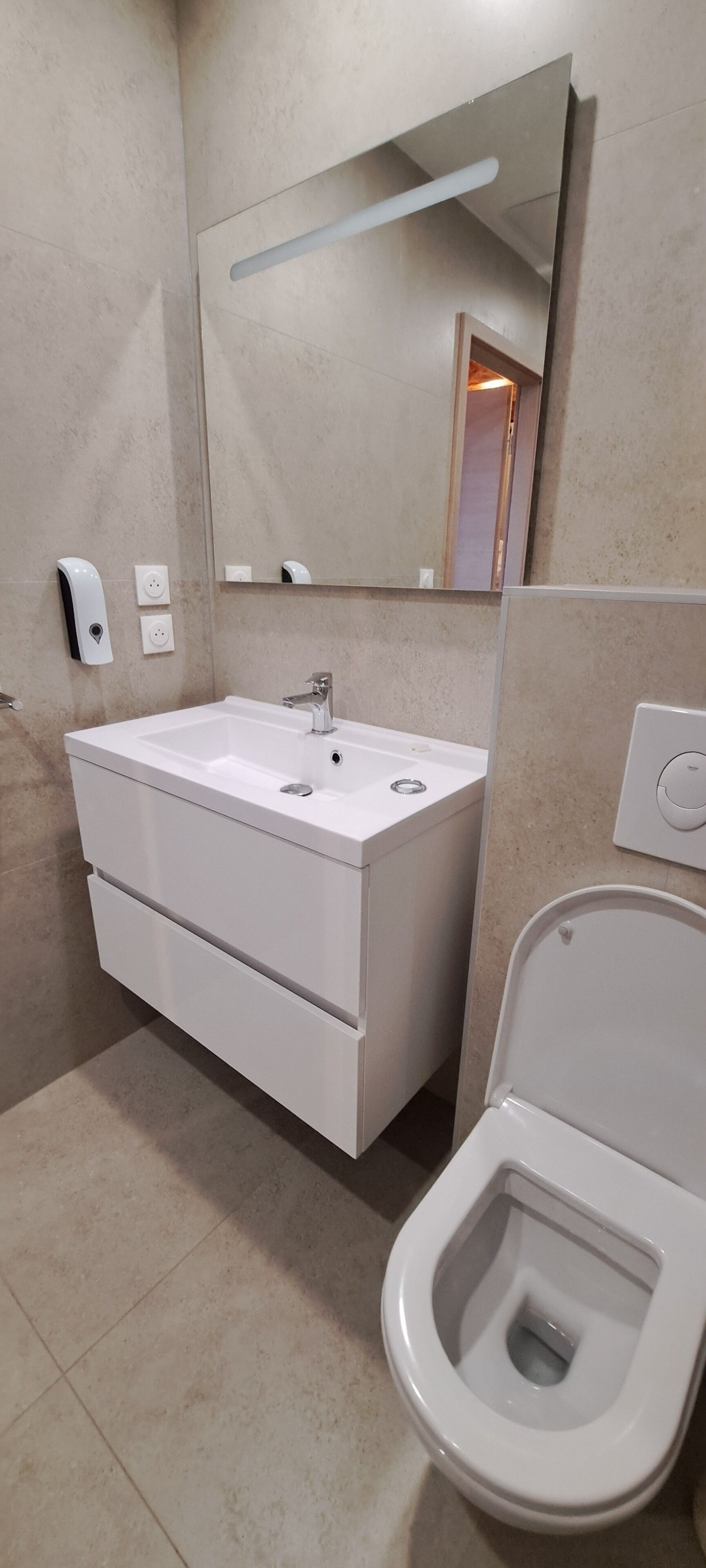 Un baño moderno con lavamanos, espejo y retrete blancos.