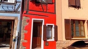 Un edificio con fachada roja, una puerta de madera y una ventana pequeña con contraventanas.