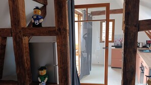 Un interior rústico con vigas de madera a la vista, una zona de cocina con armarios rosados y un vano que da a otra habitación.