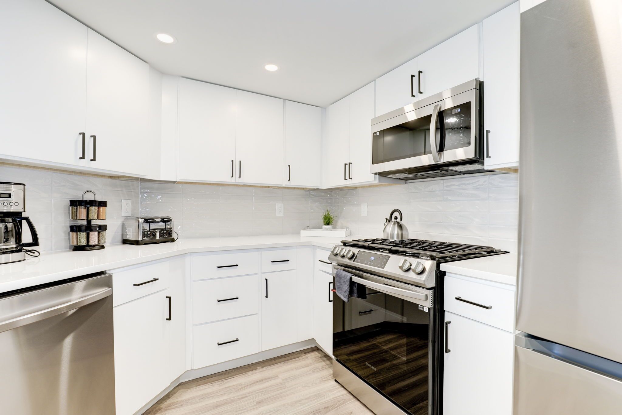 Una cocina moderna con armarios blancos, microondas integrado, estufa a gas y horno.
