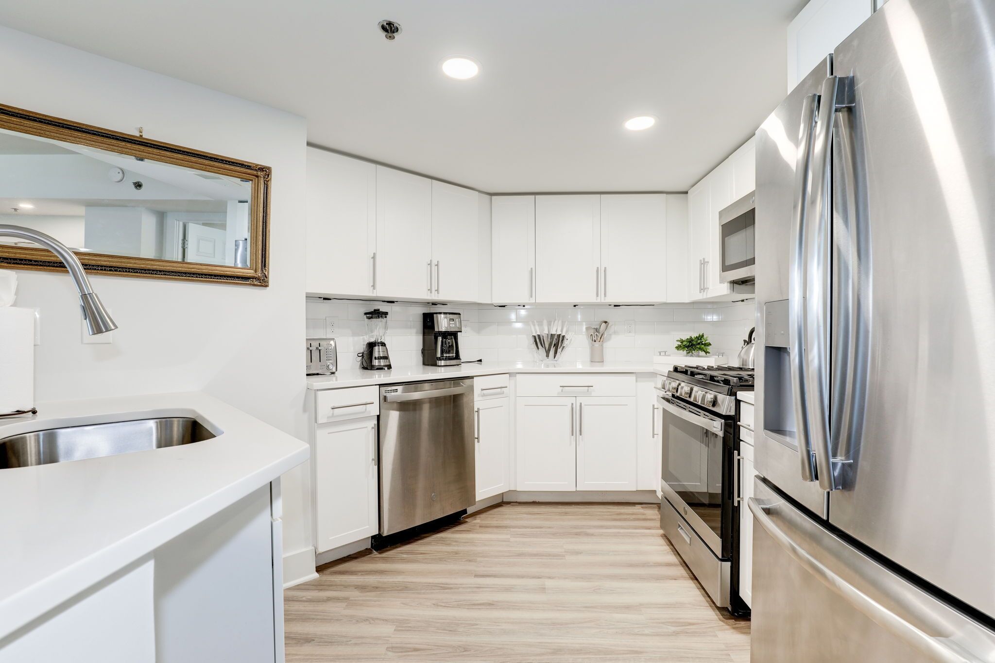 A modern kitchen with white cabinets, stainless steel appliances, and a wooden floor.