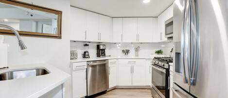 A modern kitchen with white cabinets, stainless steel appliances, and a wooden floor.