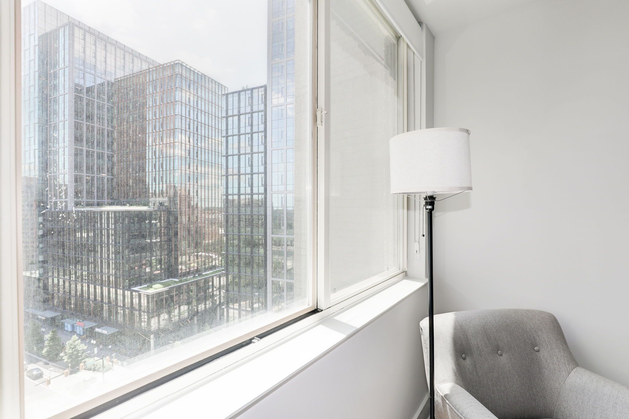A room with a large window, a grey armchair, and a floor lamp.