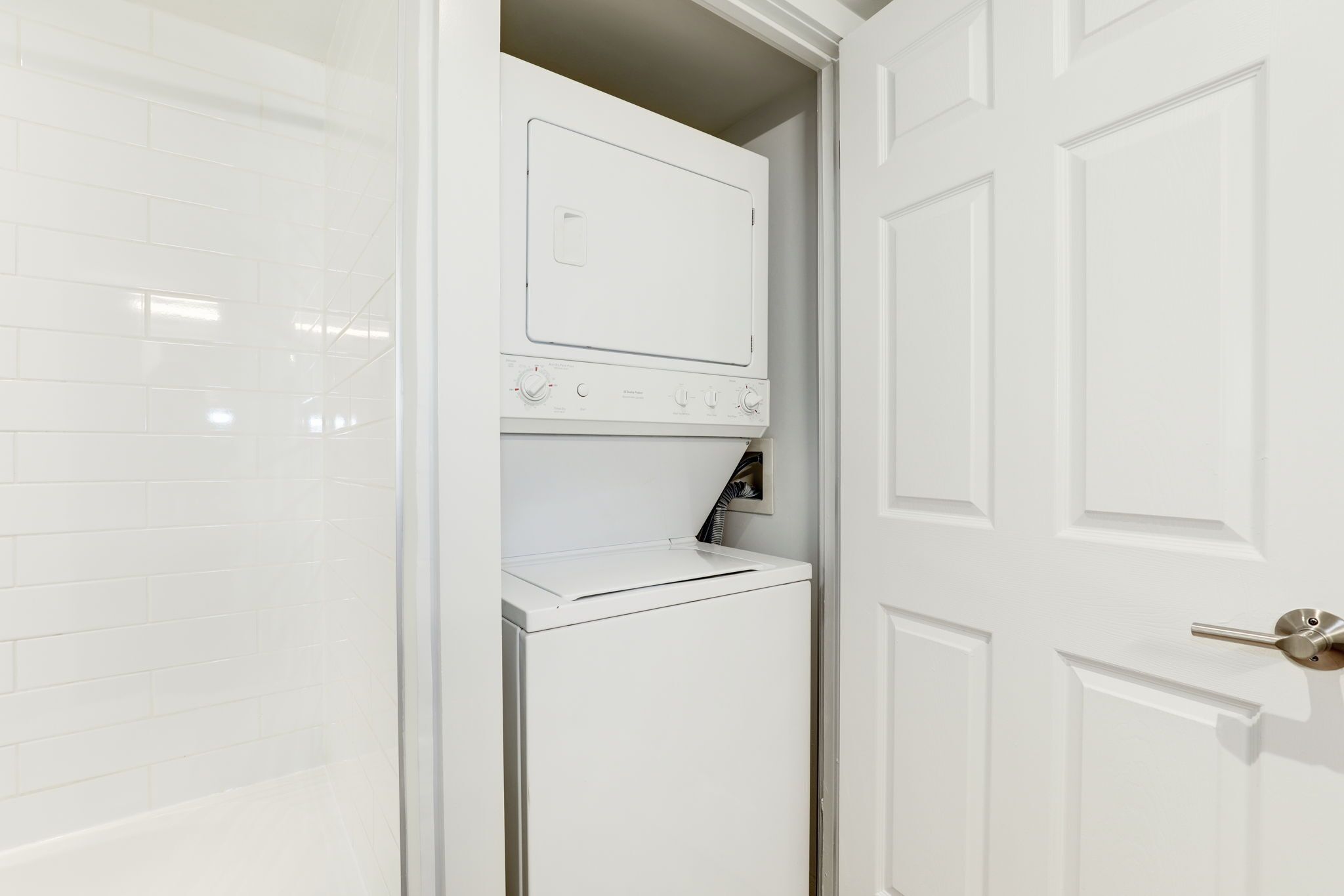A compact laundry room with a built-in washer and dryer, a door with a handle, and a tiled wall.