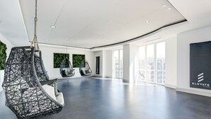 A spacious, modern interior with a large open area, two hanging chairs, and a view of the city through large windows. - Elegant 2BR Apartment Minutes From DC (Arlington)