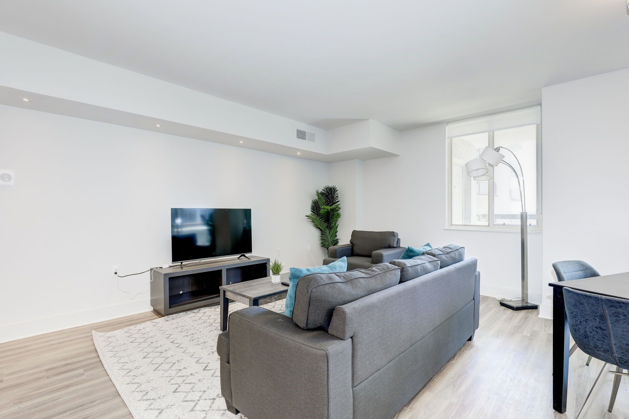 A modern living room with a grey sofa, a flat-screen TV, a coffee table, and a dining area with a table and chairs.