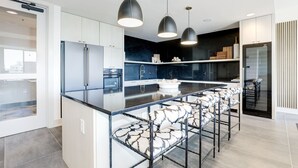A modern kitchen with a central island, bar stools, pendant lighting, and a dark backsplash. - Elegant 2BR Apartment Minutes From DC (Arlington)