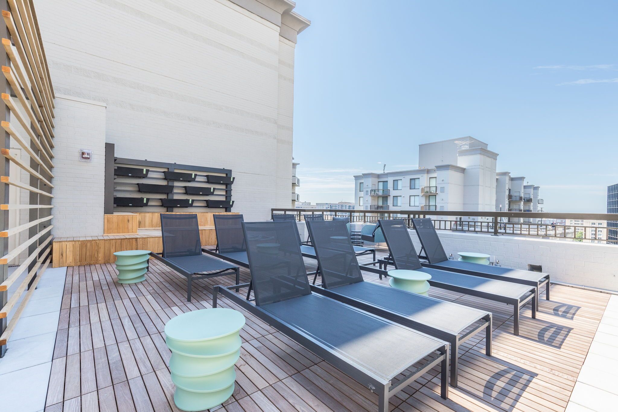 A rooftop terrace with sun loungers, a wooden deck, and a view of buildings.
