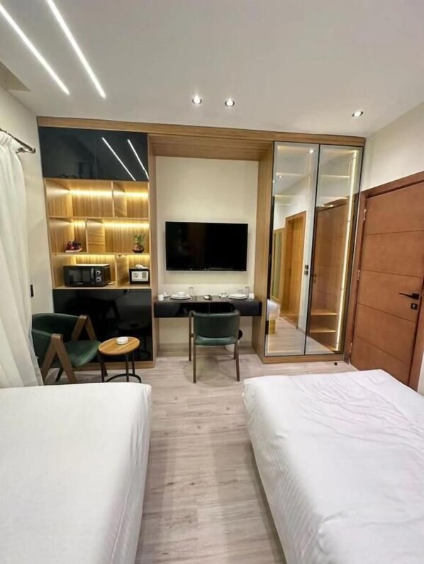 A modern hotel room with a bed, a desk with a flat-screen TV, a small seating area with a chair and table, and a wardrobe with a mirror. - Elite Boutique Hotel (New Cairo)