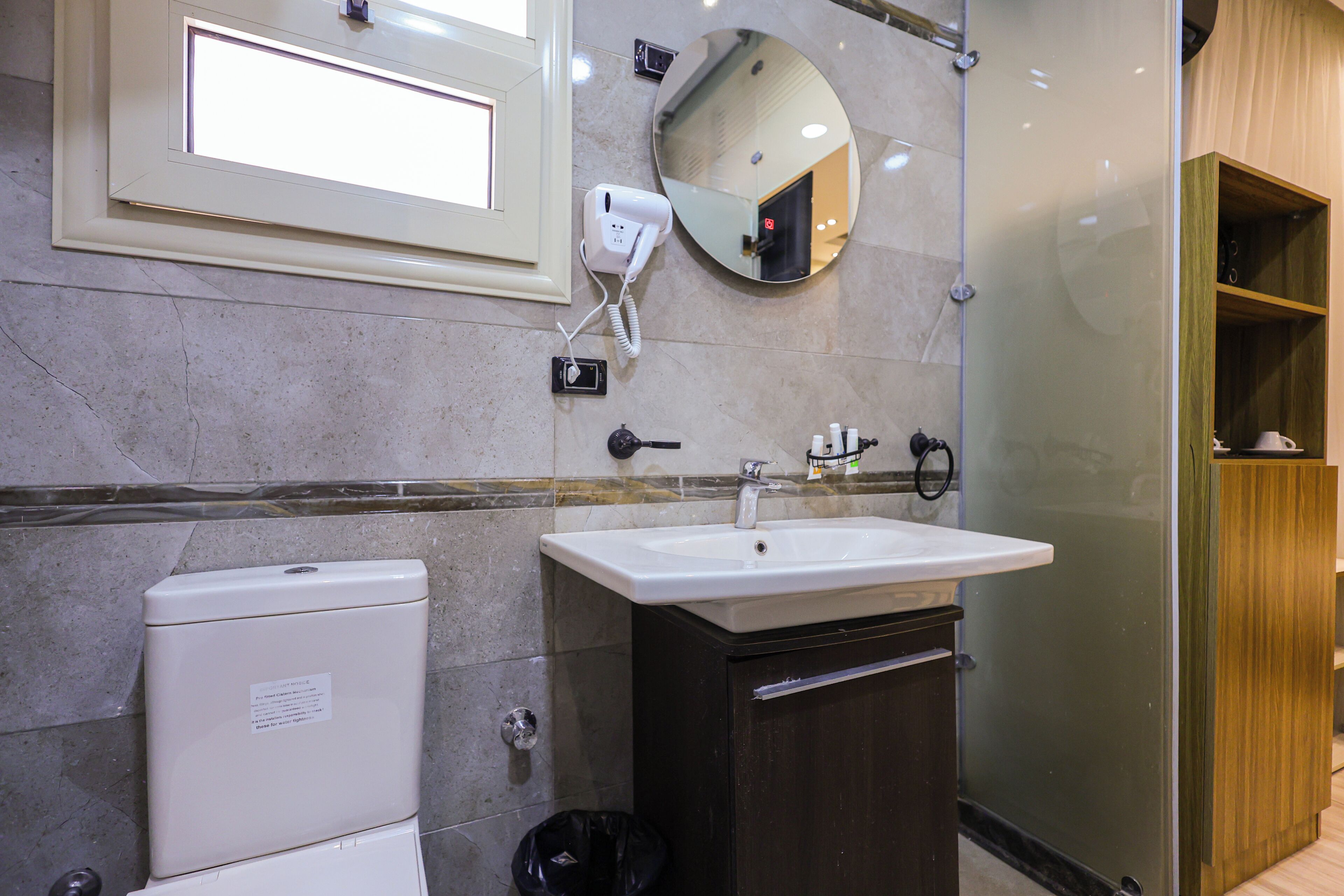 A bathroom with a toilet, sink, mirror, and a hairdryer on the wall.
