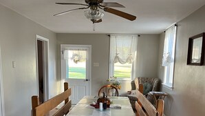 A dining area with a wooden table and benches, a ceiling fan, and windows with curtains. - Charming 3-bedroom 2 bath farmhouse surrounded by Corodus State Park in Hanover. (Hanover)