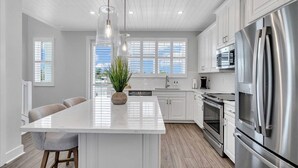 A modern kitchen with white cabinetry, stainless steel appliances, and a central island with bar stools. - Bayview Pointe! Luxury Villa near Anna Maria Island with Saltwater Heated Pool! (Cortez)