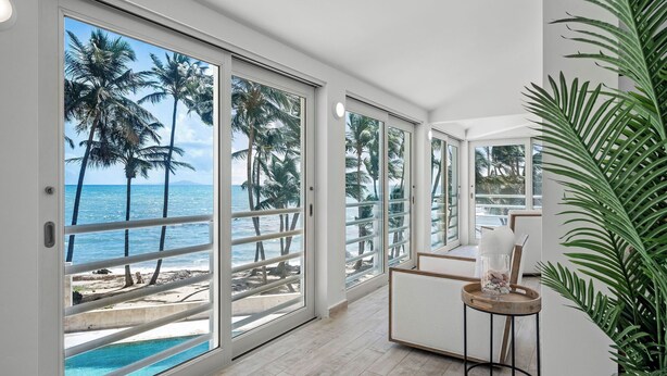 A room with large sliding glass doors leading to a beach view, a small table with a glass container, and a potted plant.